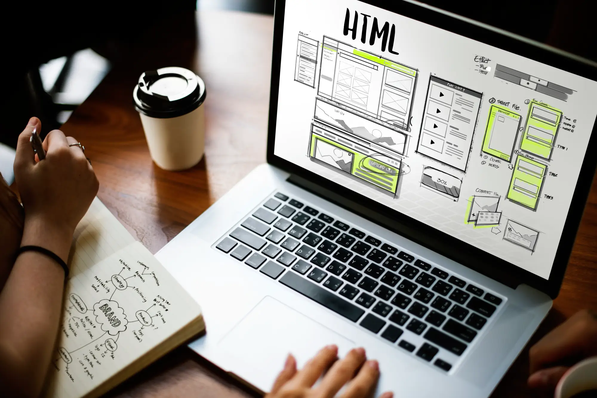 Dizajnér pracujúci na wireframoch webovej stránky s HTML štruktúrou, poznámkami v zápisníku a kávou na drevenom stole - proces tvorby webdesignu na mieru.